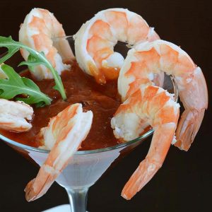 A classic Shrimp Cocktail with extra-large shrimp hanging on a martini glass filled with cocktail sauce.