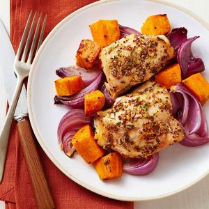 Chicken thighs roasted on a sheet pan with sweet potato chunks and red onion wedges.